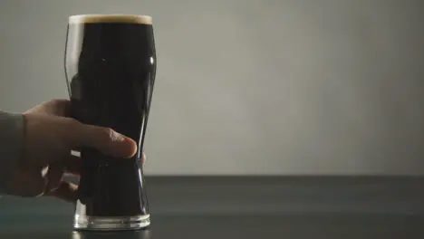 Person Picking Up Pint Of Irish Stout In Glass Against Studio Background To Celebrate St Patricks Day 1