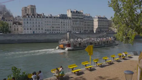 Tourist Boat In Quais De Seine Area Of Paris France With People On Banks Of River 1