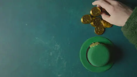 Overhead Studio Shot Of Green Leprechaun Top Hat And Hand Collecting Gold Coins To Celebrate St Patricks Day