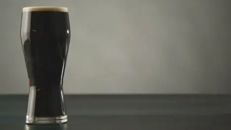 Pint Of Irish Stout In Glass Against Studio Background To Celebrate St Patricks Day