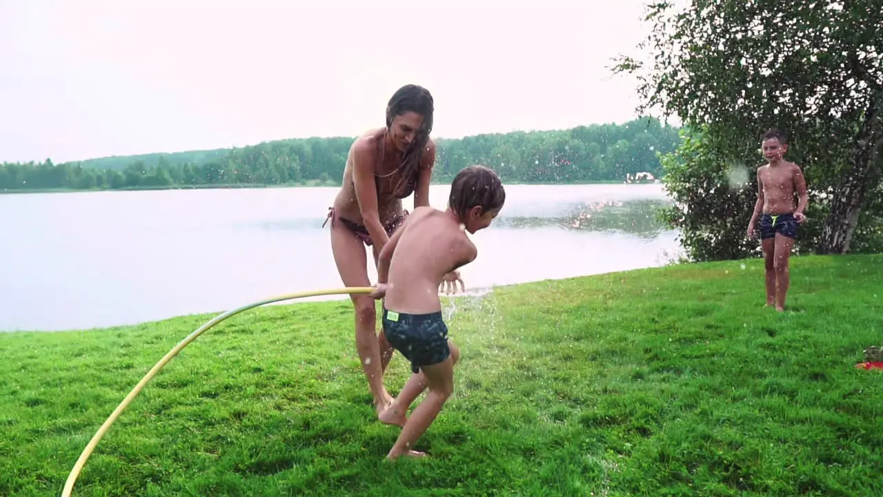 Mom dad and two sons in the summer on the grass poured water from a hose for the lawn Area country house near a lake at sunset