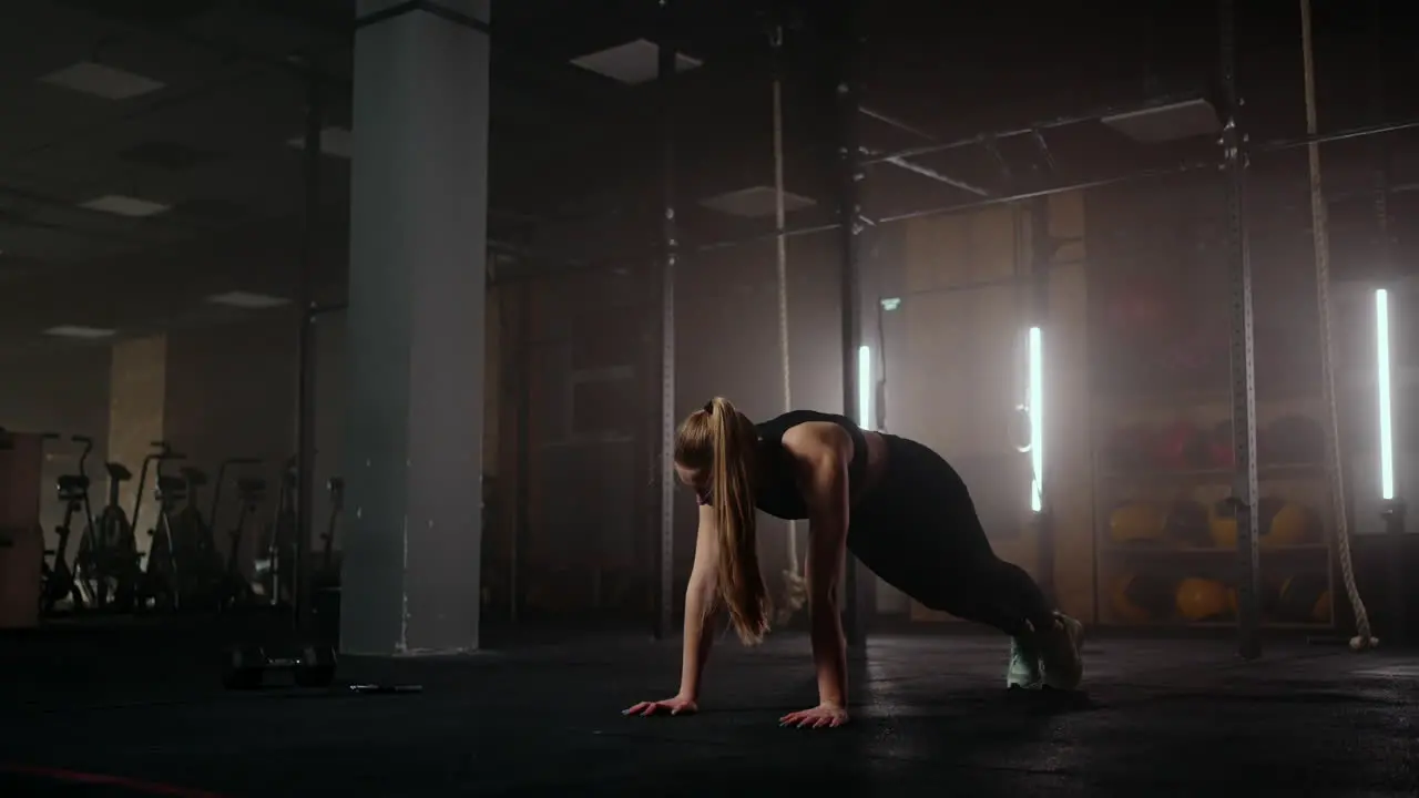 A woman does stretching exercises in a dark fitness room after a workout Fitness woman working out on core muscles at dark gym