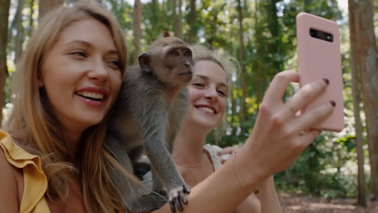 best friends using smartphone taking photos with monkey sitting on shoulder two women having fun posing with monkeys at wildlife zoo tourists travel bali