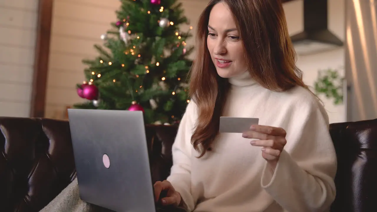 Happy Woman Shopping Online Using Credit Card While Sitting On The Sofa Near A Christmas Tree In The Living Room At Home 1