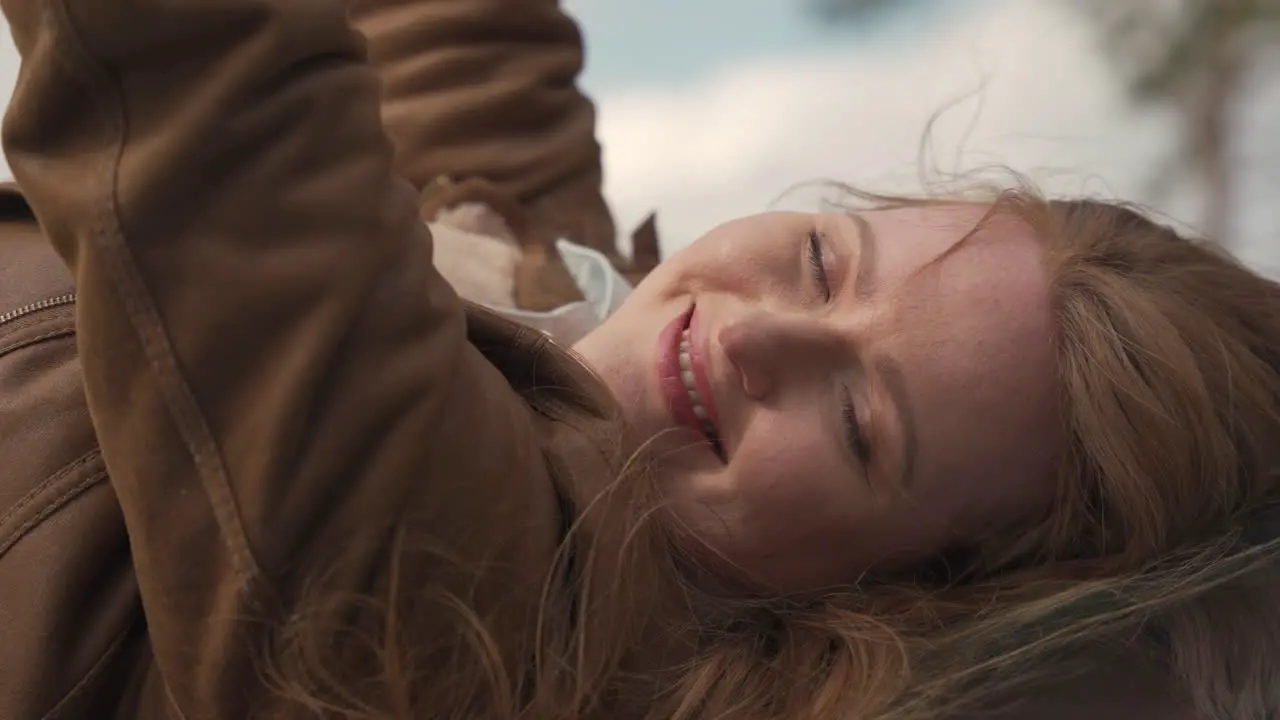 Portrait Of A Beautiful Smiling Red Haired Woman Lying Outdoors Looking Directly At The Camera