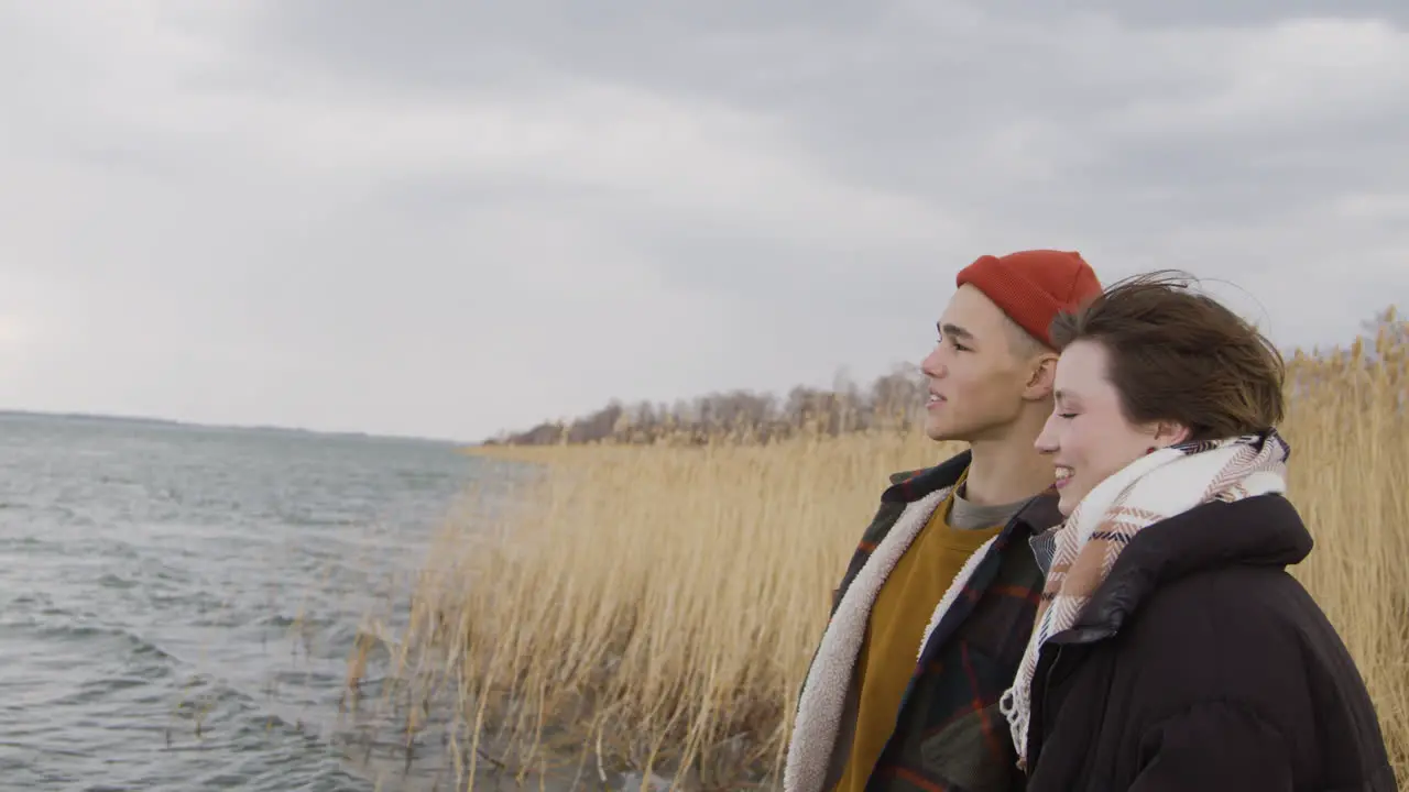 Side View Of A Teenage Boy And Teenage Girl Talking Standing Near Of Seashore On A Cloudy Day