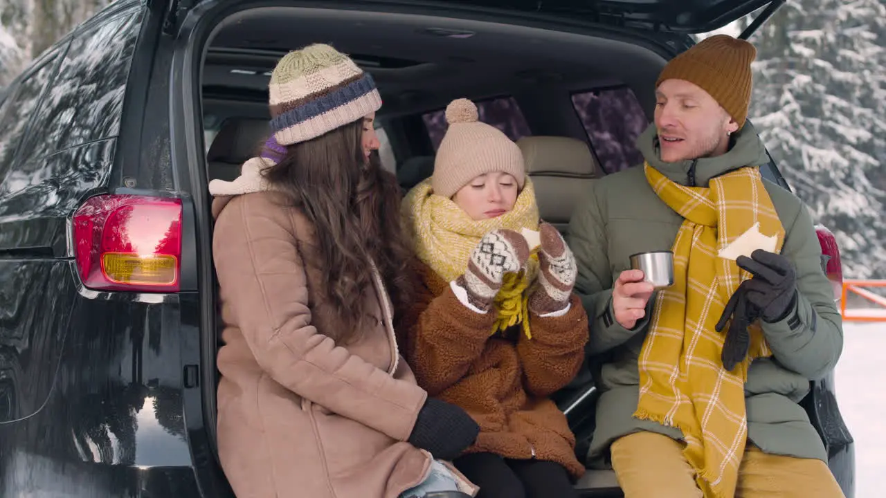 Parents And Daughter Eating Sandwiches And Drinking Hot Drink Sitting In The Trunk Of The Car In A Snowy Forest 2