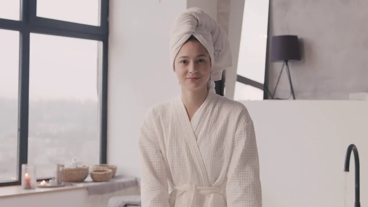 Front View Of A Woman Sitting Posing And Smiling At The Camera With A Towel On Her Head And A Bathrobe