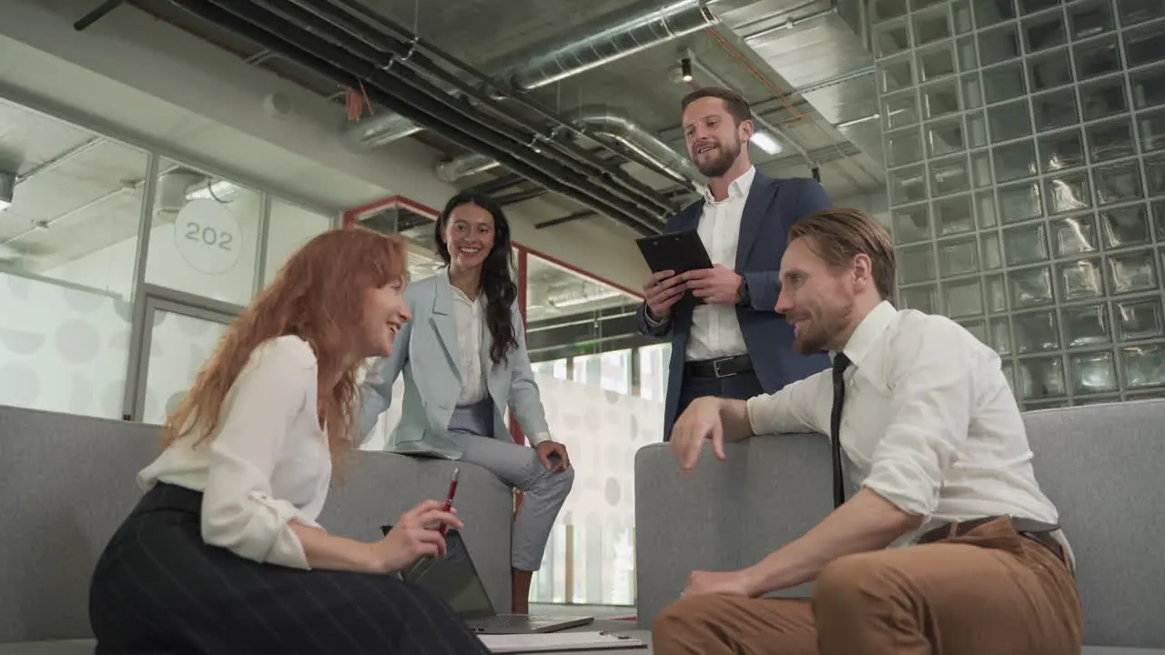 A Business Working Group Consisting Of Two Women And Two Men Have A Relaxed Meeting In The Armchairs In The Common Area Of The Offices 5