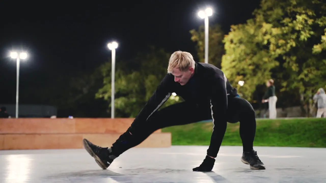 Sportive Blond Man Stretching Legs Before Training In The Park At Night 1