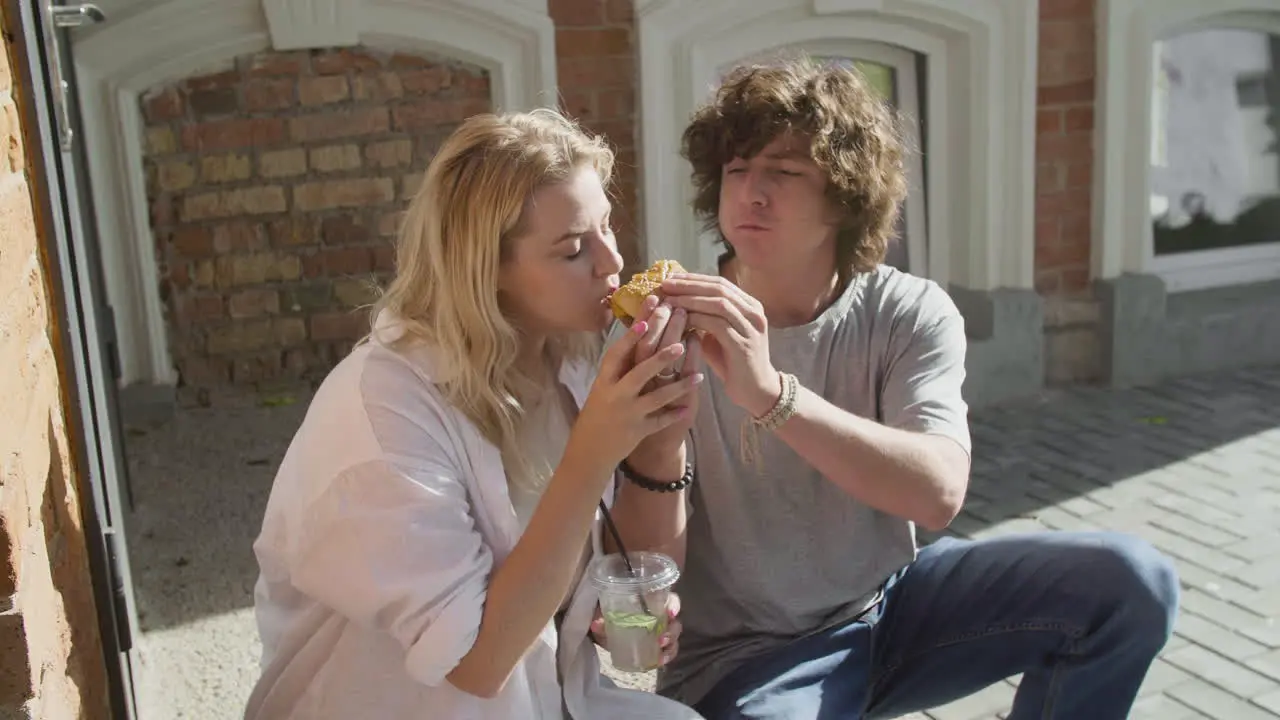 Pareja Joven Compartiendo Una Deliciosa Hamburguesa Y Bebiendo Una Bebida Fría Juntos Sentados En La Acera