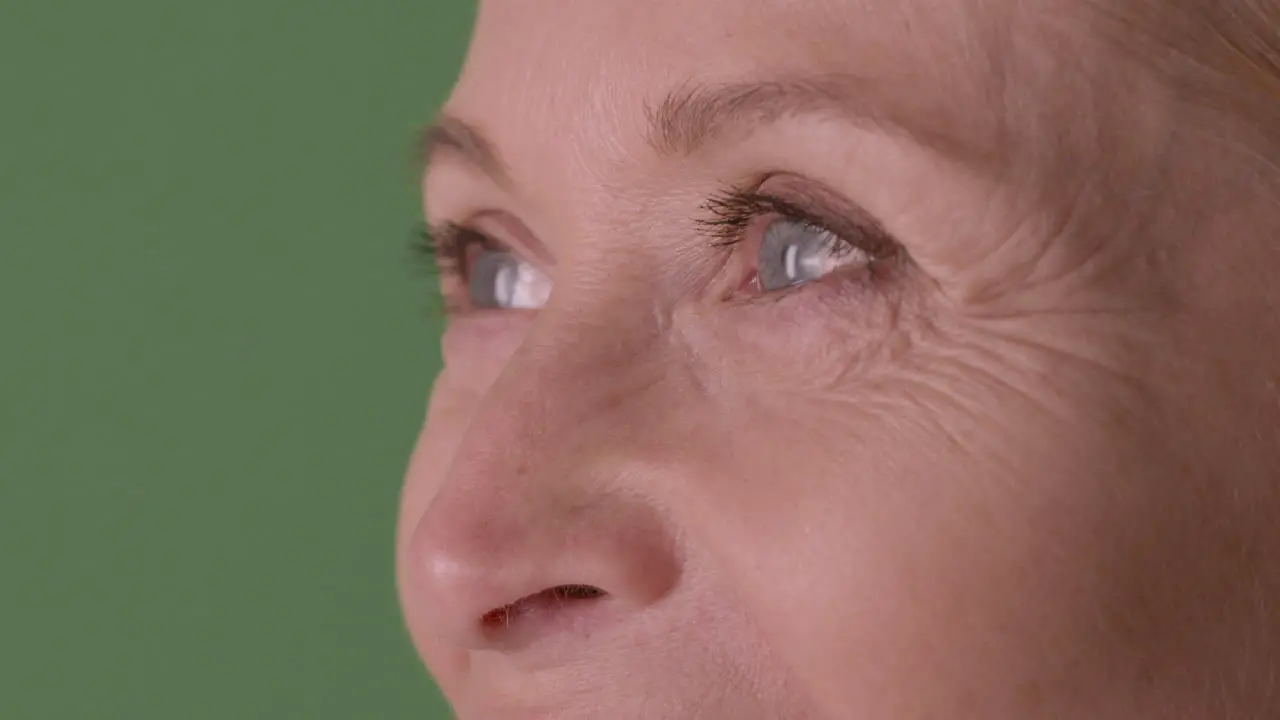 Vista De Cerca De La Mitad De La Cara De Una Mujer Madura Rubia Con Ojos Azules Sonriendo Y Mirando Al Costado Sobre Fondo Verde