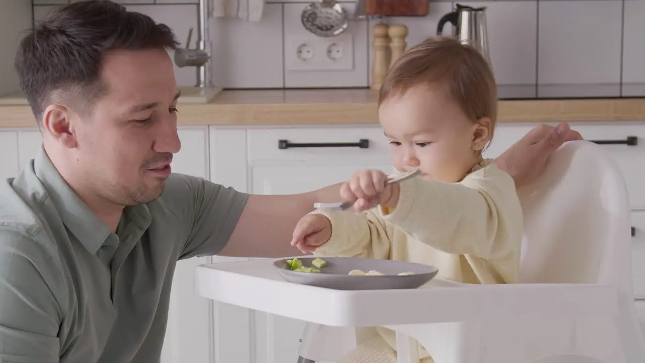 Süßes Kleines Mädchen Das Im Hochstuhl Sitzt Gabel Hält Und Mit Essen Spielt Während Ihr Vater Sie Ansieht