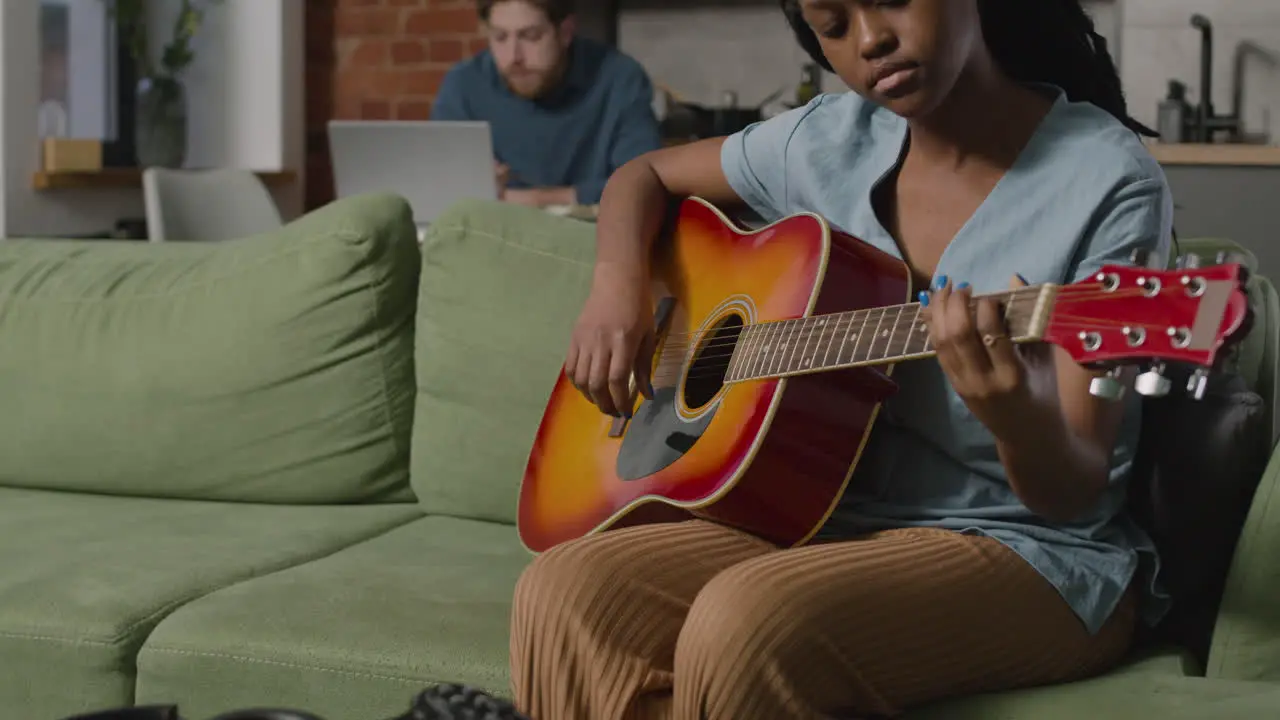 Mädchen Das Gitarre Spielt Sitzt Auf Dem Sofa Während Ihr Männlicher Mitbewohner Den Computer Benutzt 1