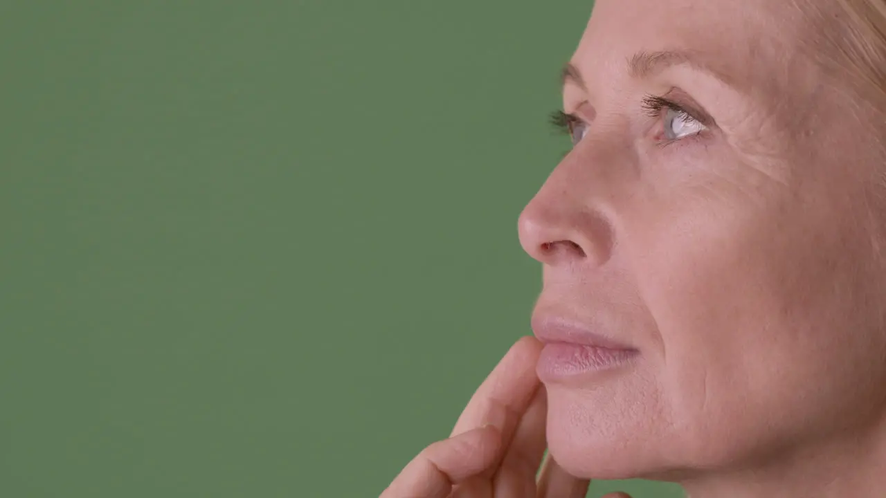 Vista De Cerca De Una Mujer Madura Rubia Con Los Ojos Cerrados Tocándose La Cara Y Mirando Al Costado Sobre Fondo Verde