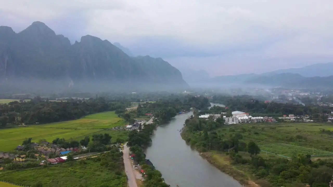 Aerial Evening View Of Vang Vieng With Nam Xong River Running Through Misty Landscape