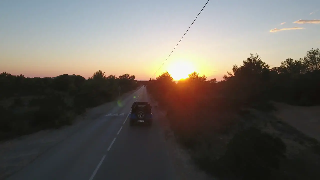 Drone shot following a car driving on a road through trees