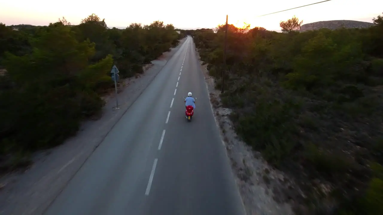 Drone shot following a scooter on a road through trees