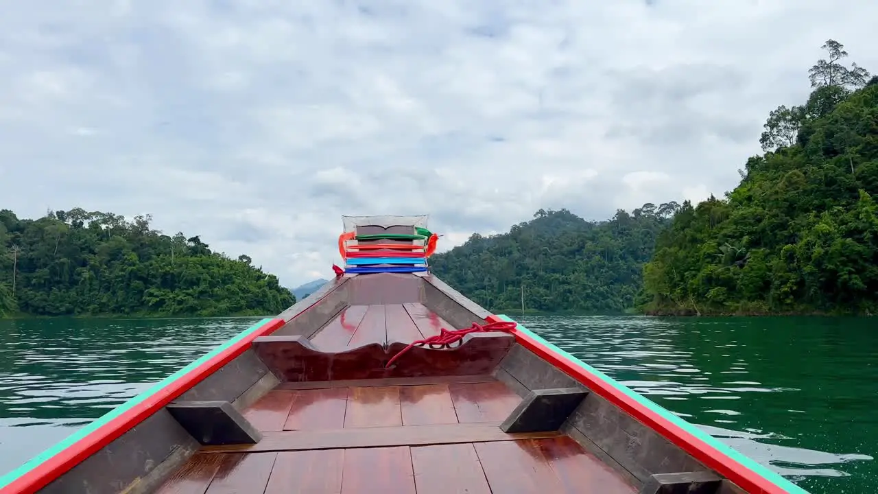 Boat glides Khao Sok Lake showcasing front water jungle and mountains