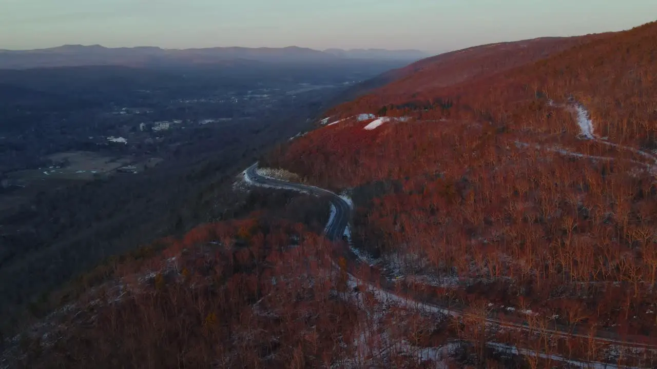 Flying over a scenic highway on a mountain high above a vast valley during winter just after sunset with a little snow on the ground