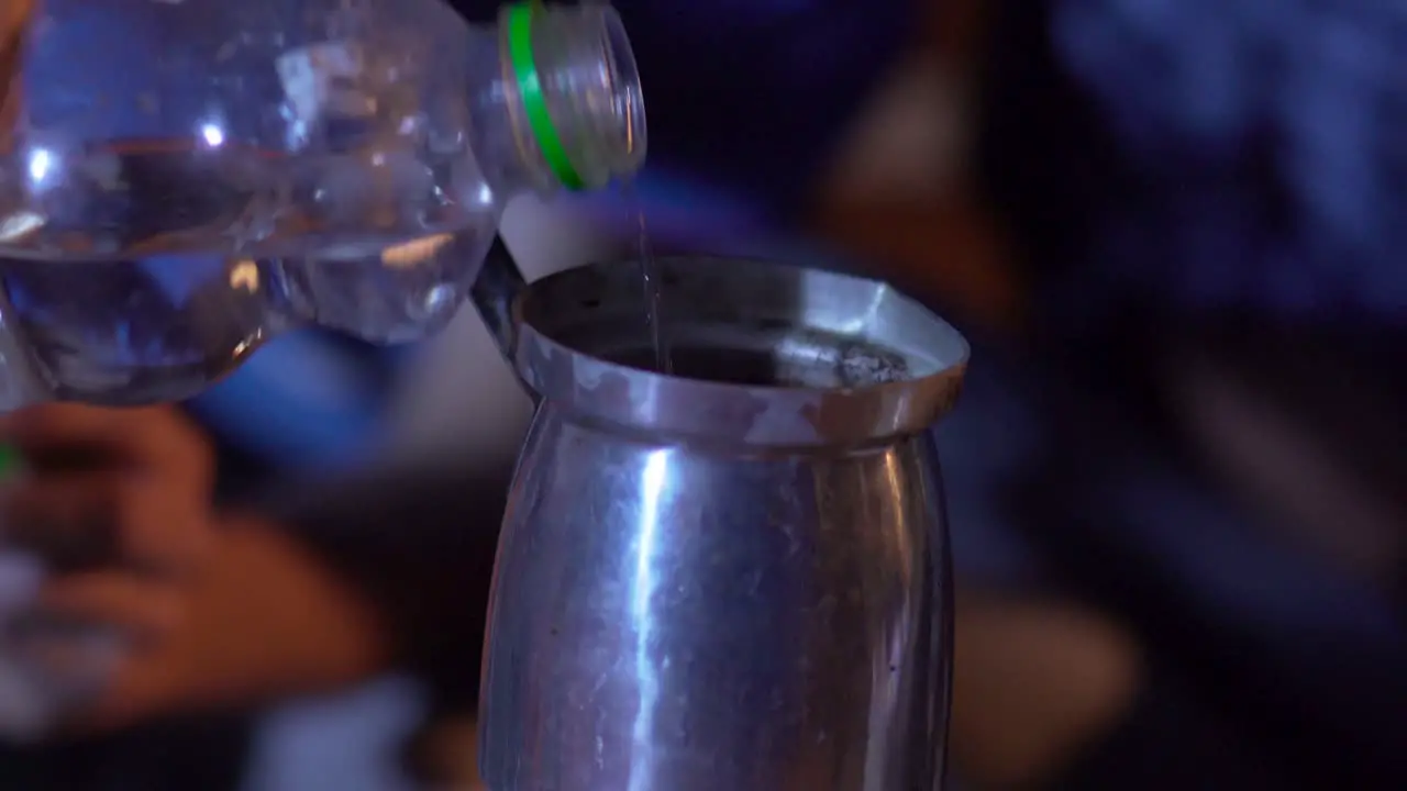 Close up pours water from a bottle into the pot Tilt down to fire under the pot