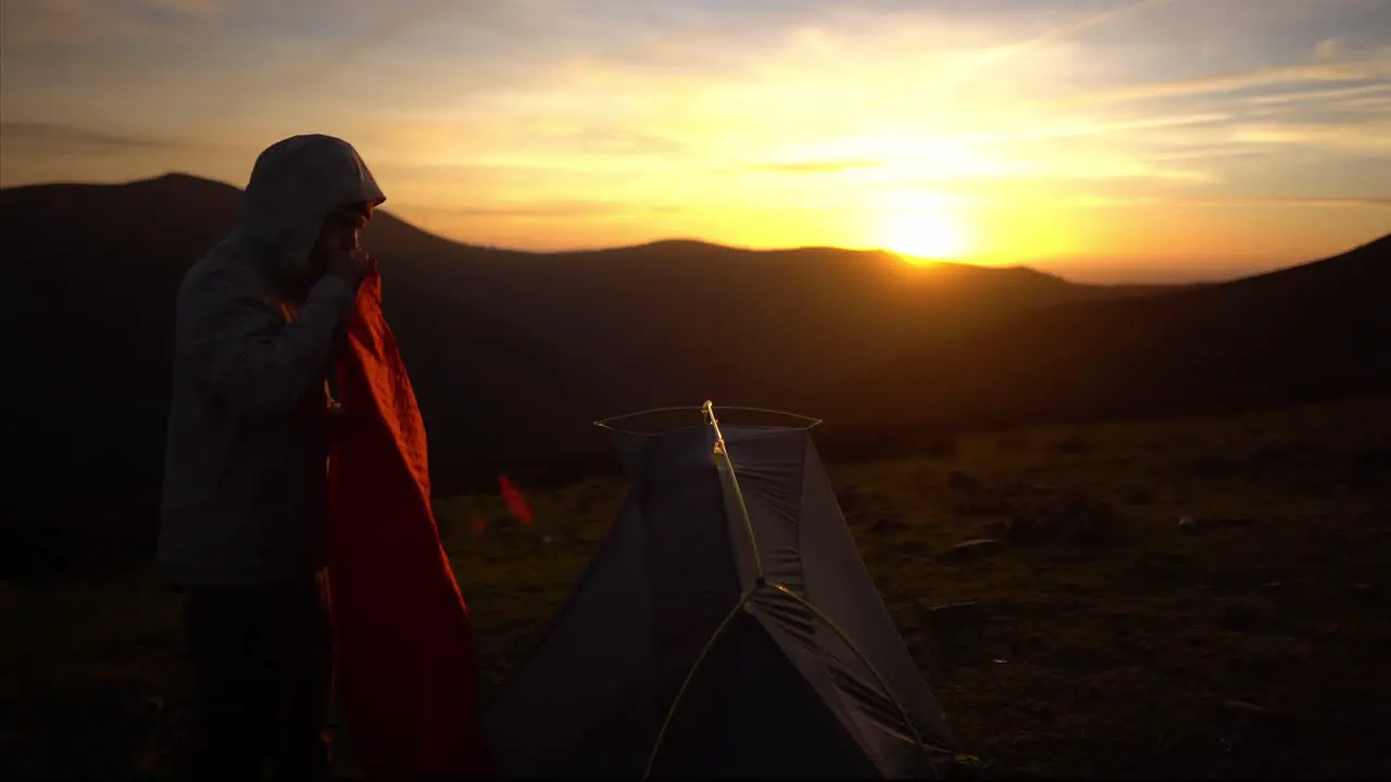 Young hiking man prepares campsite tent for nature camping at sunset