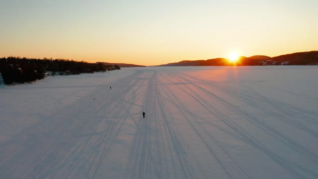 Aerial view of people snowshoeing and dogs running along a frozen river as the sun sets