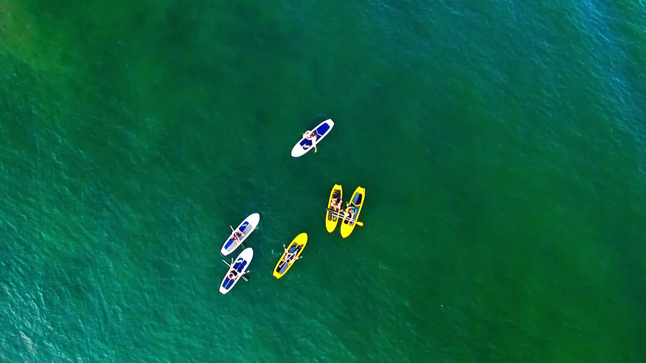 A group of young friends hang out on paddle boards on the water drone shot