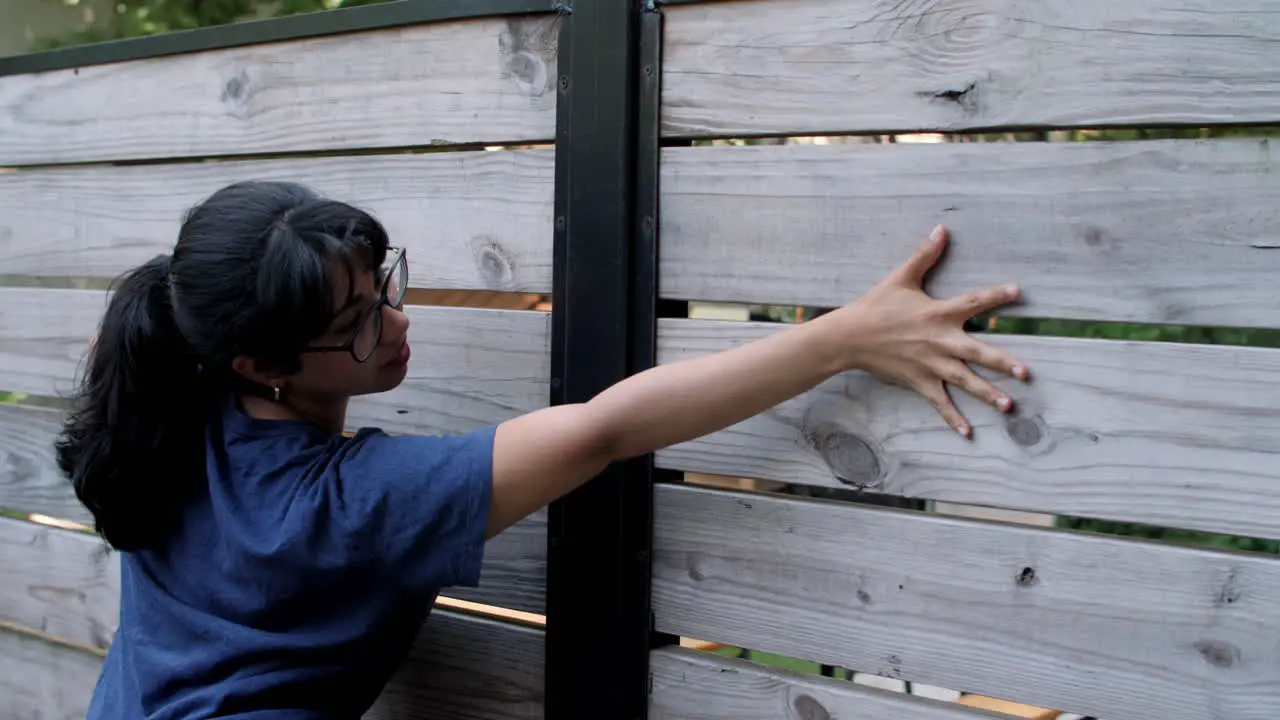 A young Latina woman wearing glasses caresses a wood fence