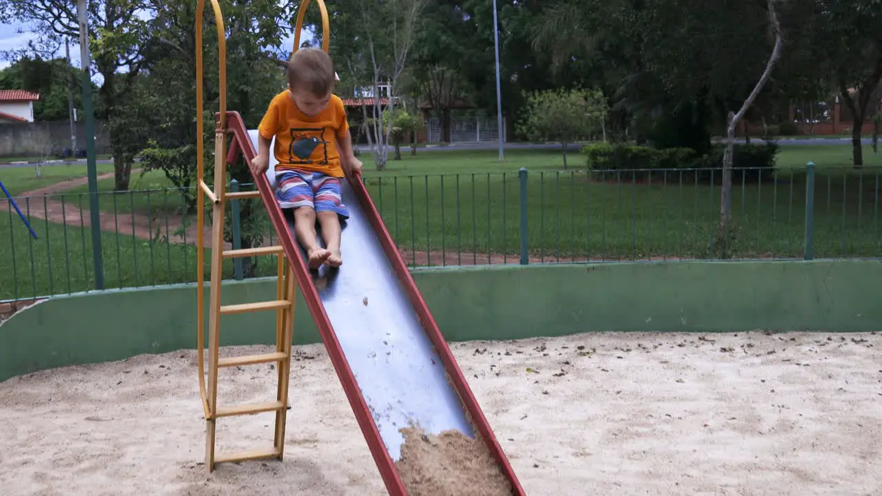 kid climbing up and then sliding down the slide with sand on the end during a bright day with trees in the background