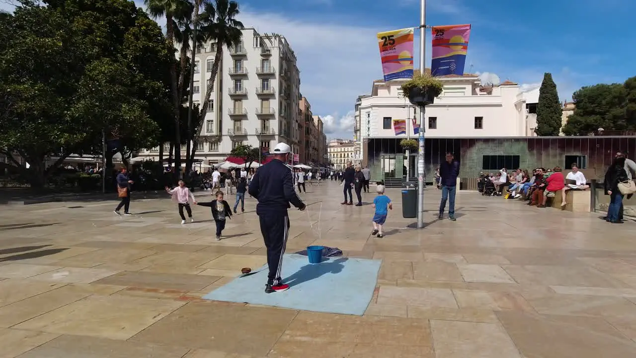 Male street performer using string to create soap bubbles and plays with kids