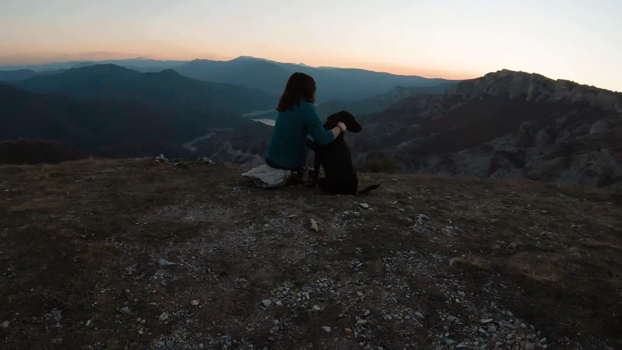 Girl sitting and cudling black labrador dog on a mountain