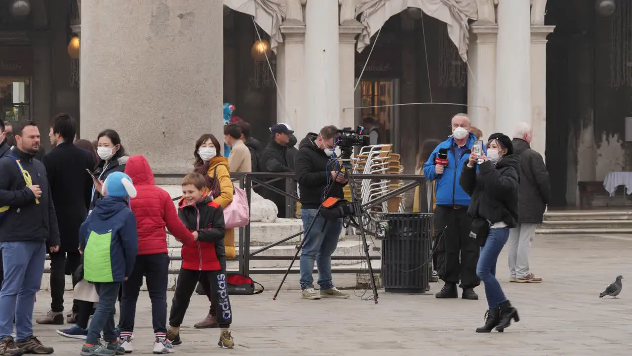 Reporter and Cameraman Wearing Protective Face Masks in St Mark's Square Venice After the Cancelled Carnival People Passing By