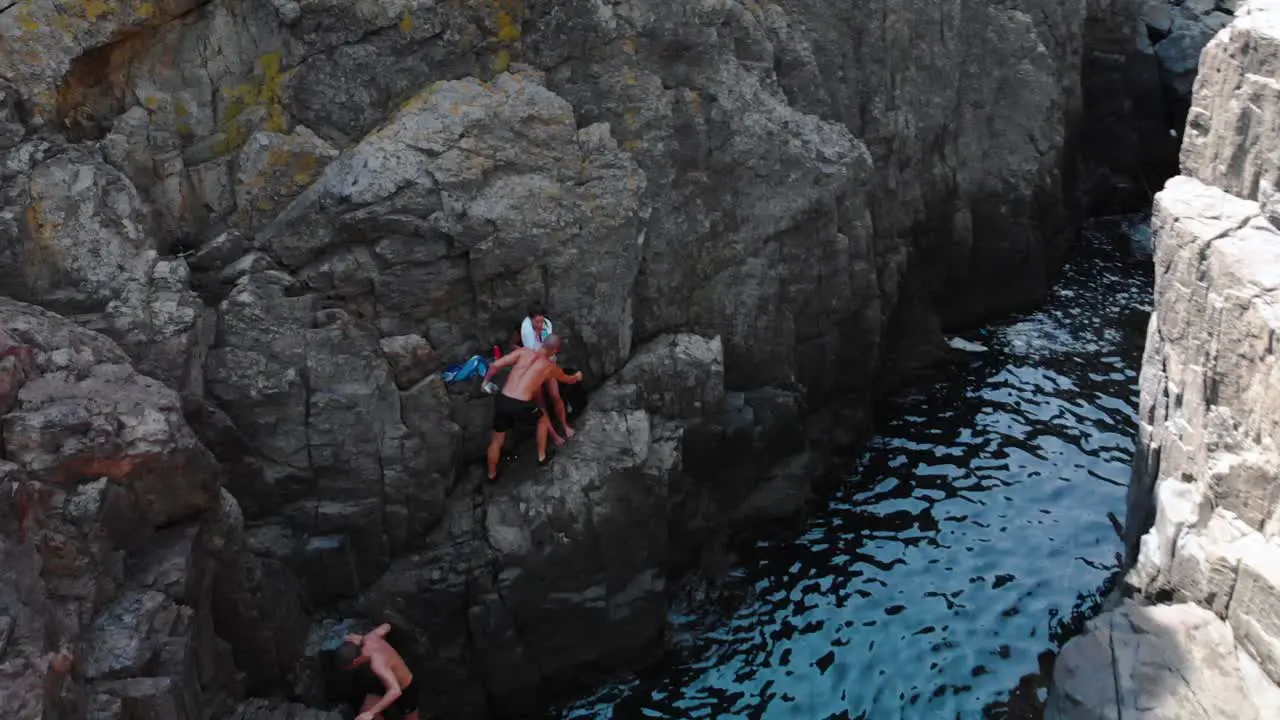 Aerial shot of two boys and girl on high seashore cliffs after diving summer time