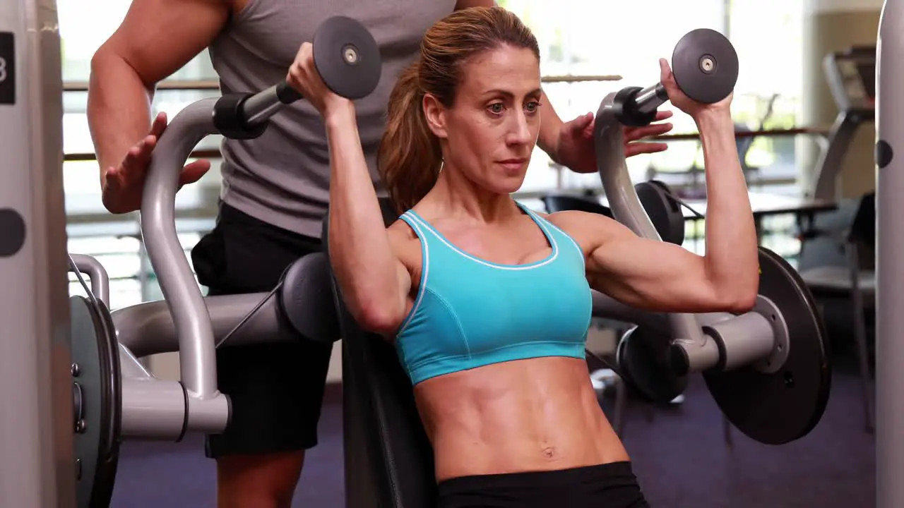 Fit woman using weights machine for arms with her trainer