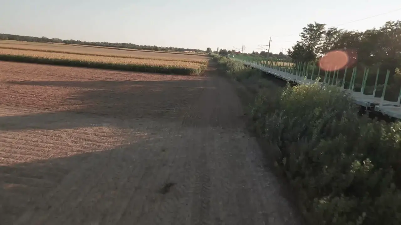 Aerial drone footage captures an empty cargo train journeying through expansive golden-lit cornfields with the drone flying overhead showcasing the rural landscape