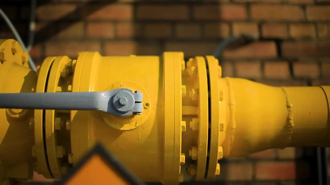 Close-up of a bright yellow gas pipeline with flanges set against a brick wall highlighting industrial infrastructure