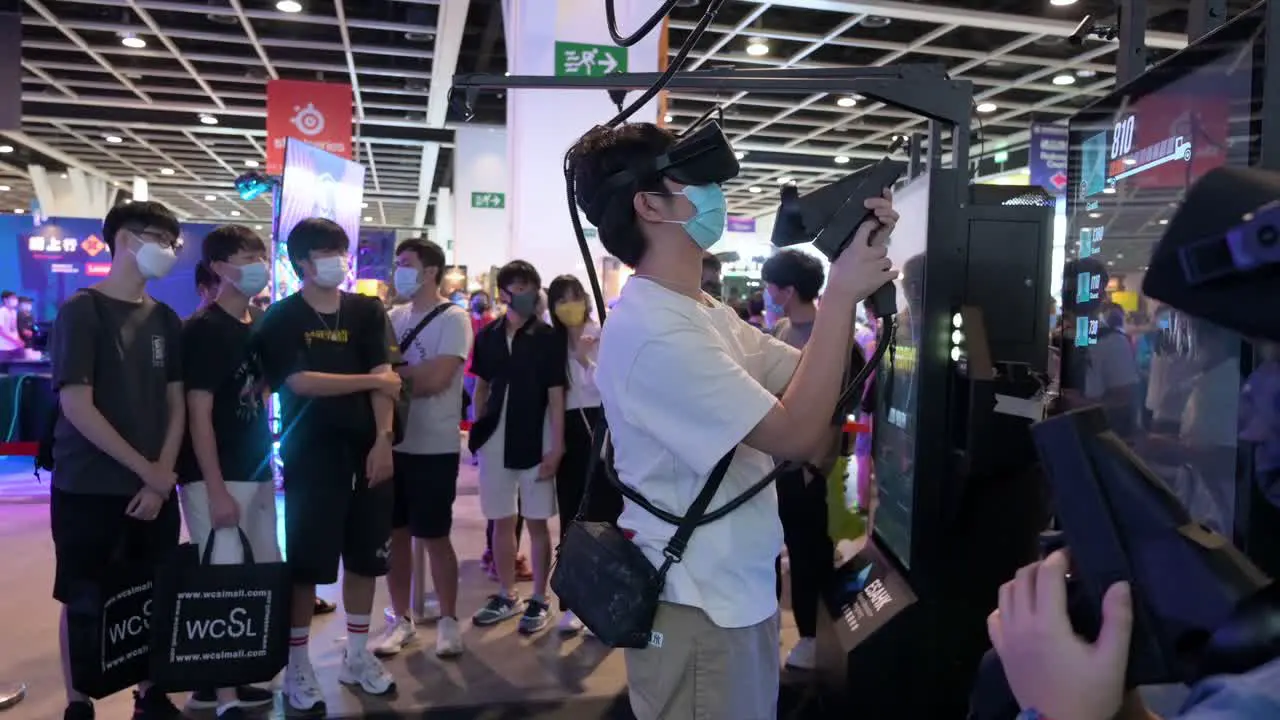 Chinese young gamers play Virtual Reality shooting videogame while other visitors queue and wait their turn to play during the Hong Kong Computer and Communications Festival in Hong Kong