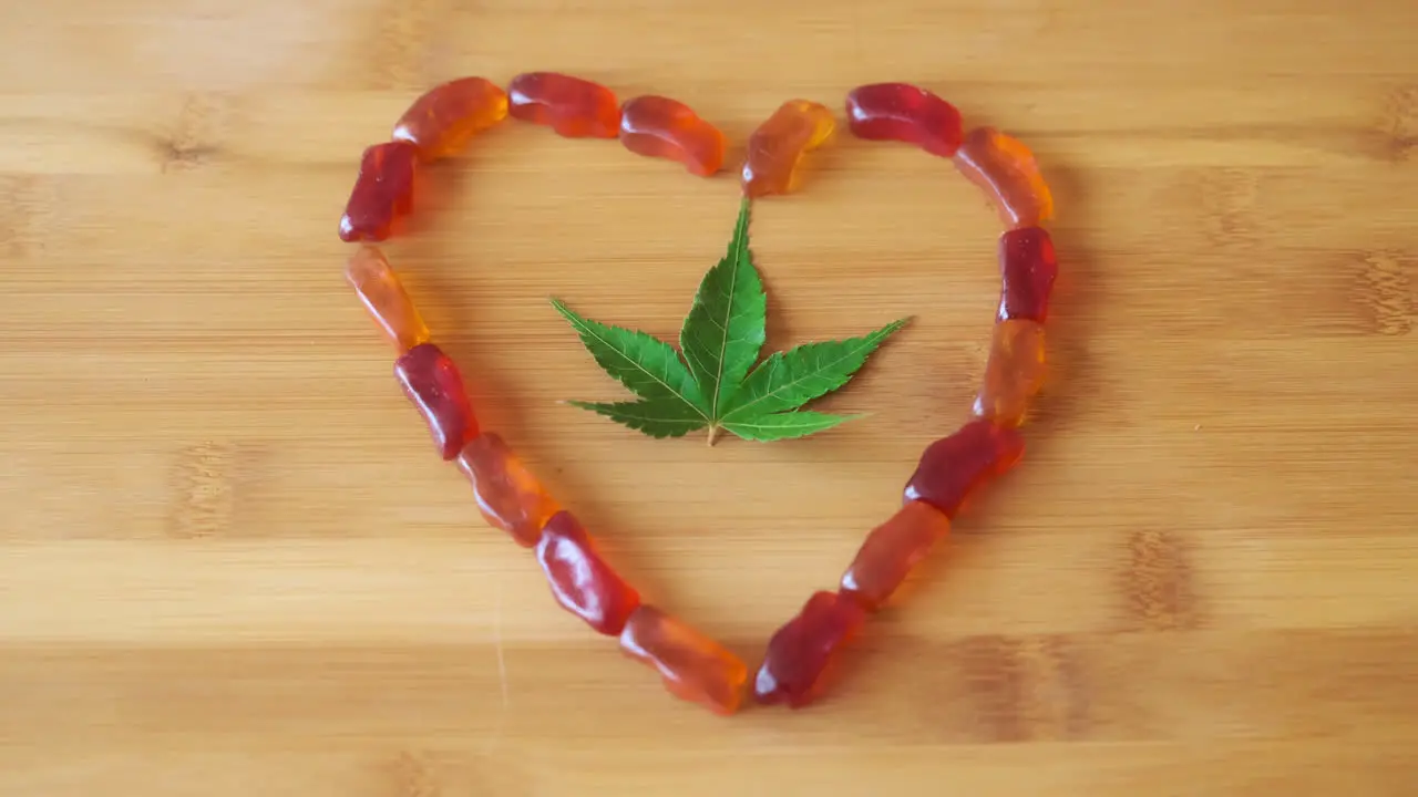 Slow Motion Hand Picking up CBD Gummy from Gummy Heart with Marijuana Leaf in Center