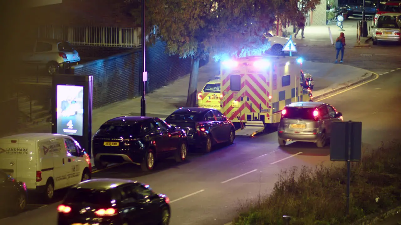 A London bus drives past an ambulance with flashing lights at night England