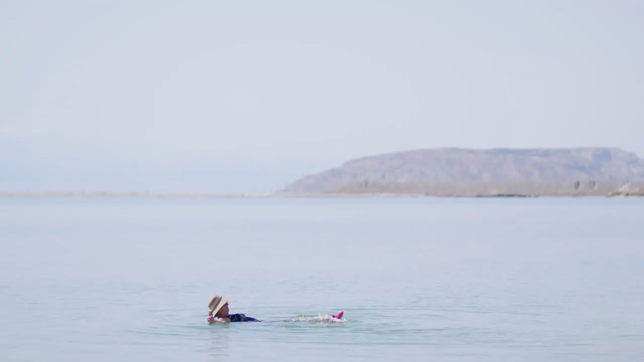 An elderly tourist with a hat floats on her back in the Dead Sea Israel and enjoys leg movements