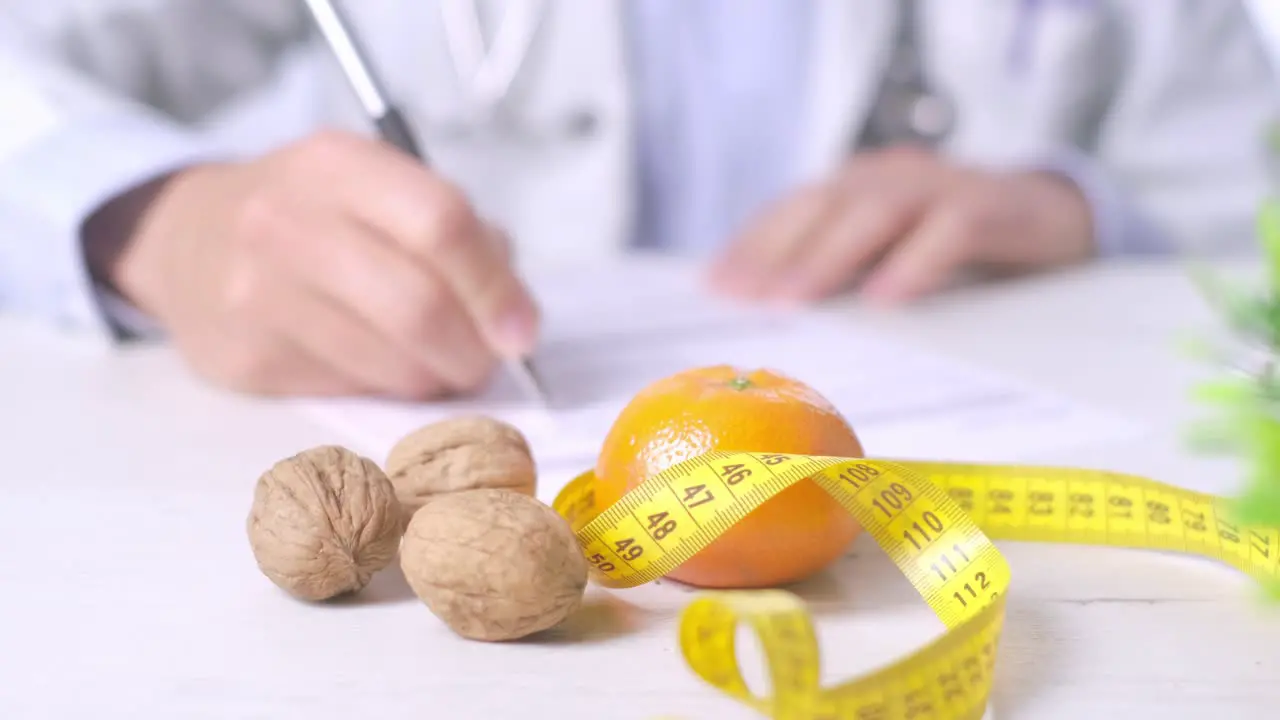 Close-up shot of nutritionist writing a Diet prescription Walnuts tangerine and measuring tape on table