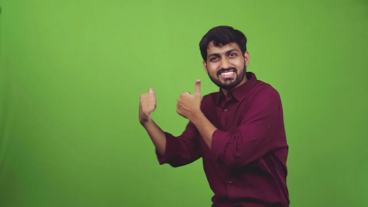 Attractive young man showing something behind him with thumbs isolated on green screen