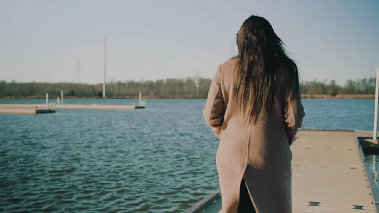 Footage of a woman walking along a lake dock on a chilly day at sunset