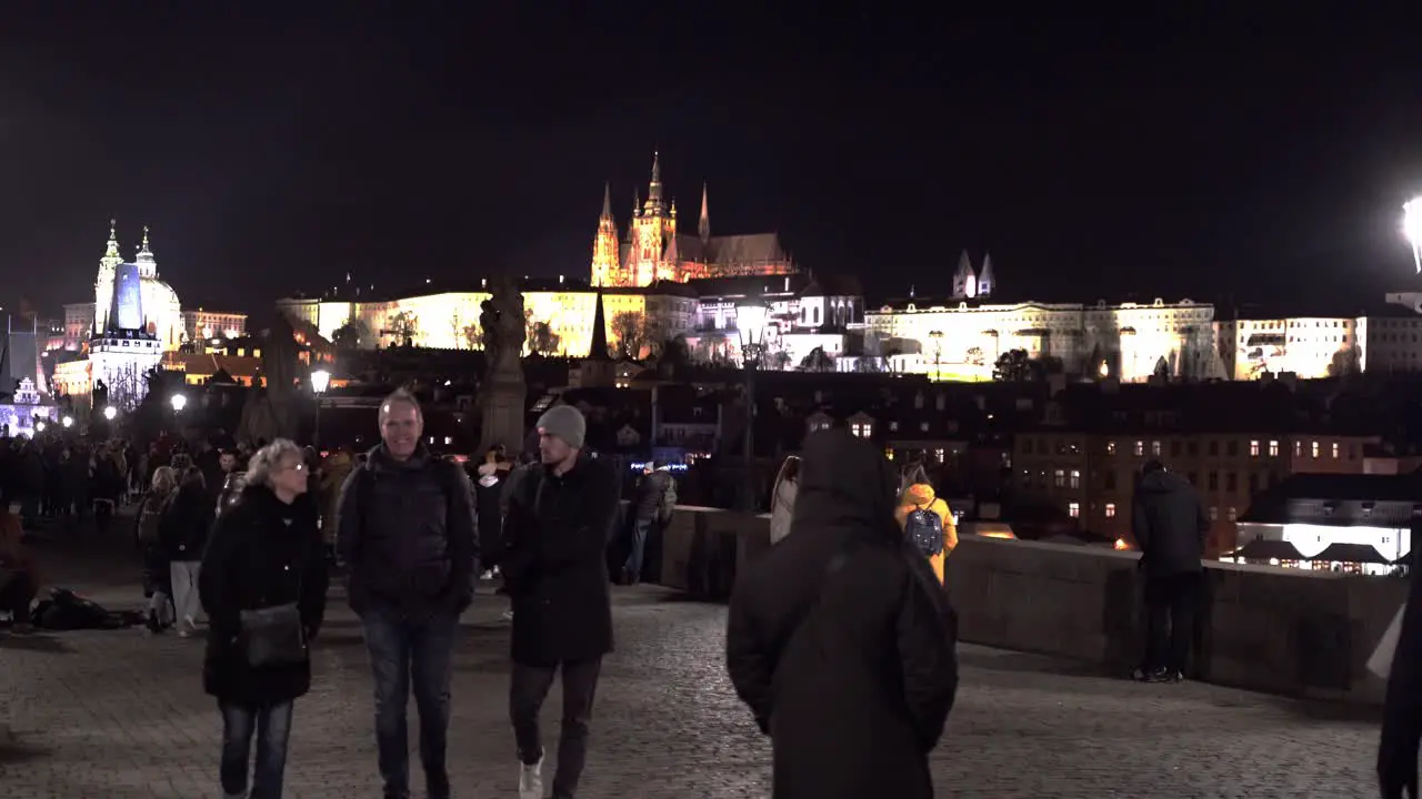 People walking on Charles bridge on winter night Prague castle beyond