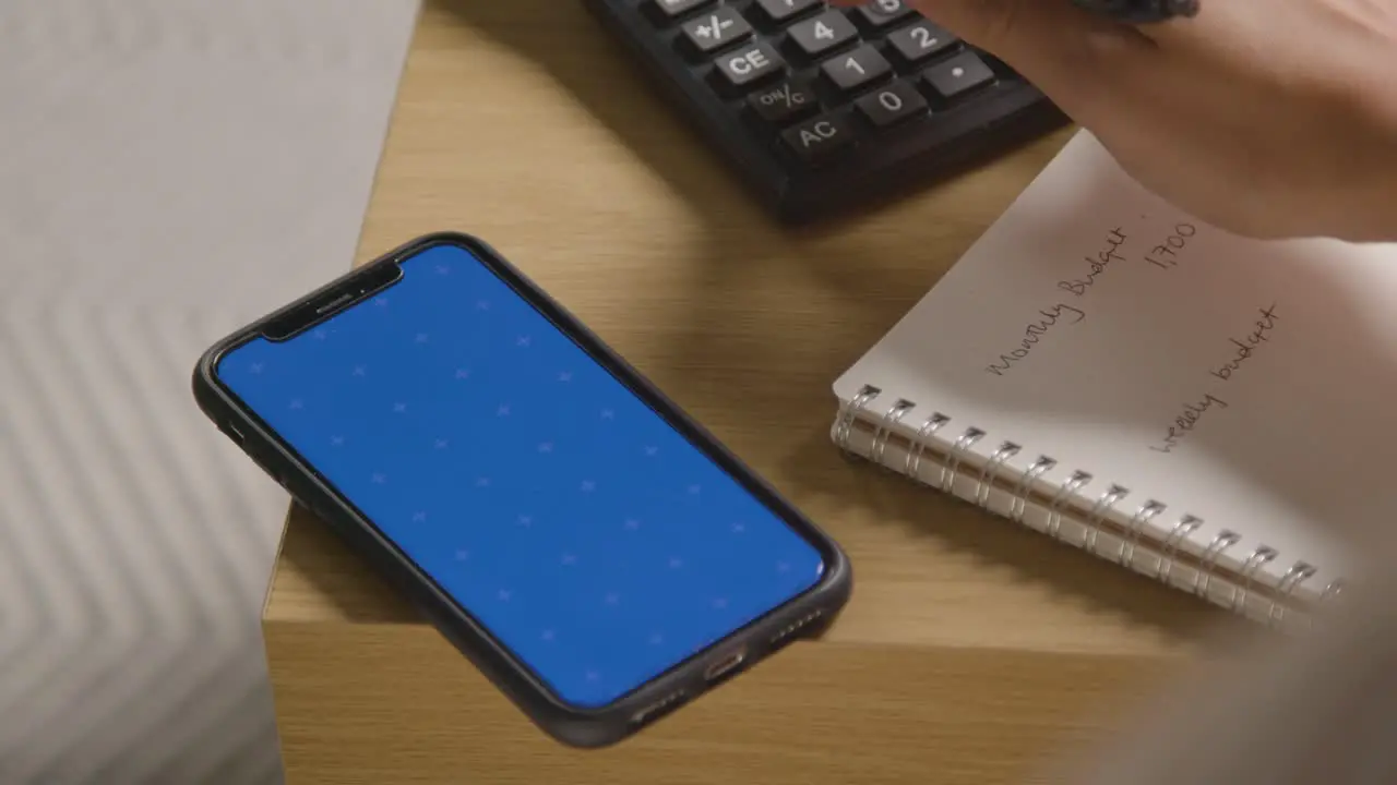 Woman Using Blue Screen Mobile Phone And Calculator To Check Household Budget In Cost Of Living Crisis 2