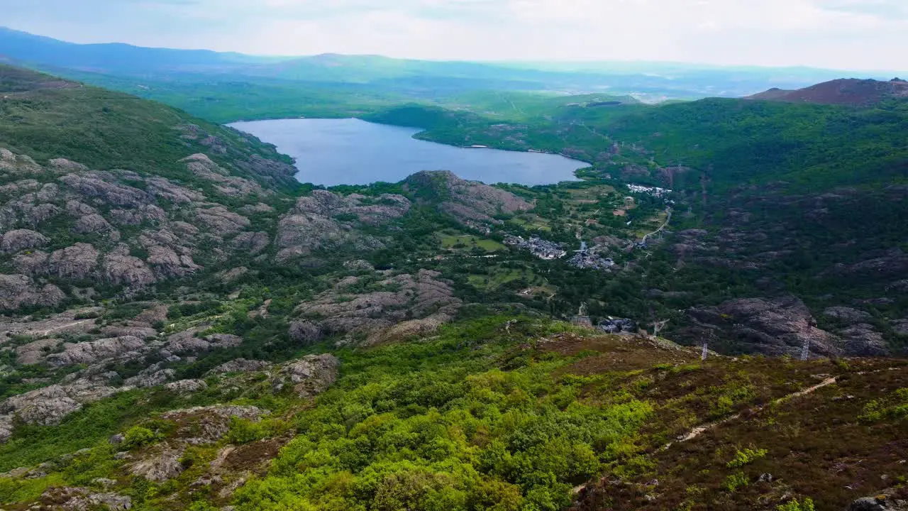 Aerial dolly push in above green hillside reveals sanabria lake in distance