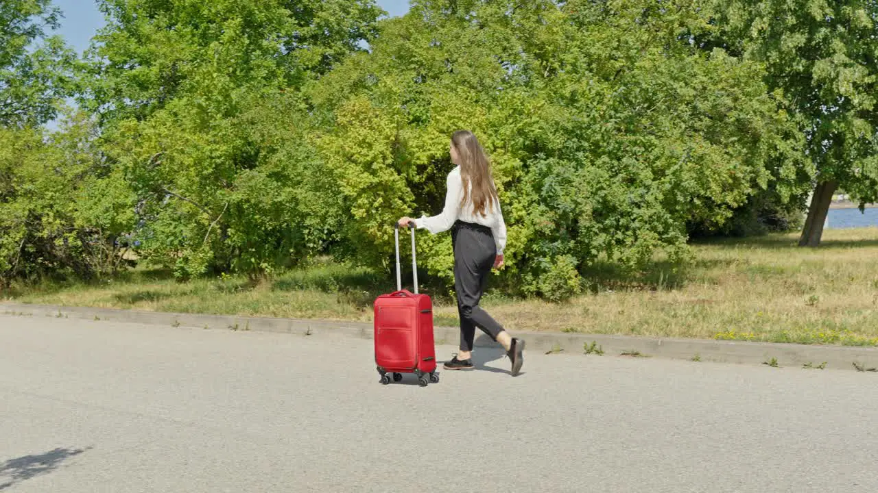 Girl walking through green park in slow motion with red luggage Riga