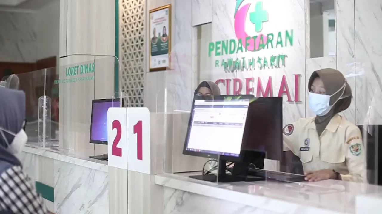 An old woman registers in the patient registration room and is served by the clerk or nurse at the hospital registration