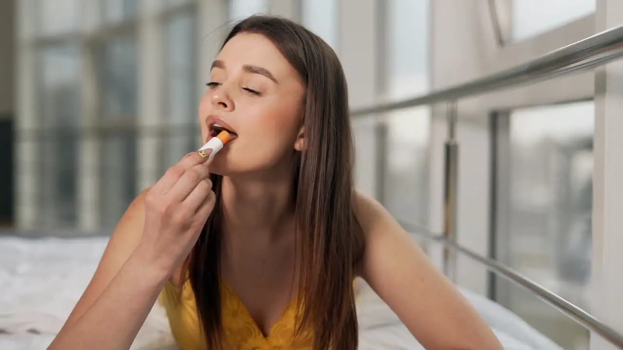 Portrait of a beautiful girl in yellow pajamas applies hygienic lipstick on the lips